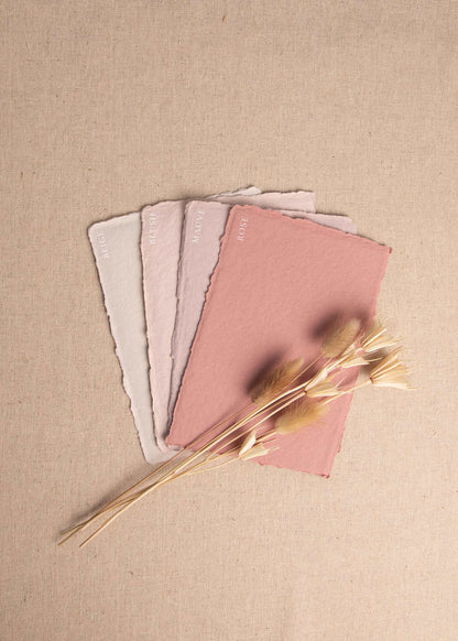 Fanned pile of Beige, Blush, Mauve, Rose handmade paper envelopes with deckle edge surrounded by dried flowers