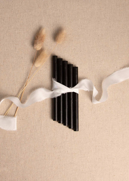 Black wax sealing sticks on linen background wrapped in white silk ribbon with dried flowers