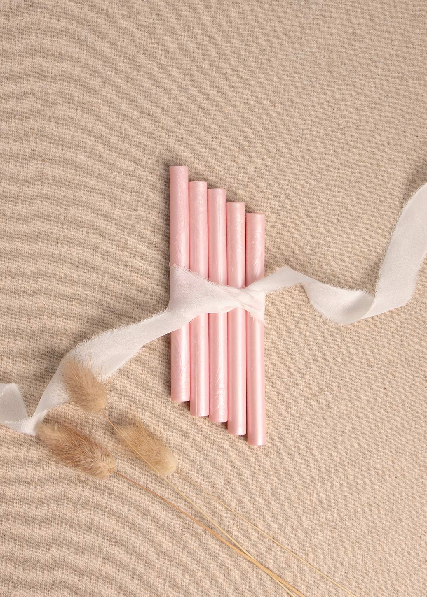 Champagne pink wax seal sticks on linen background with white silk ribbon with dried flowers 