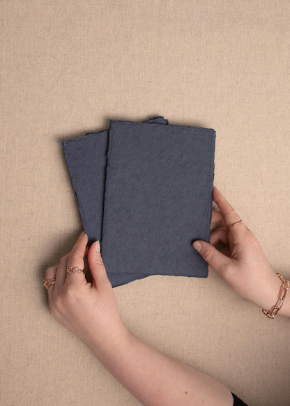 Elevated view of woman’s hand holding dark blue 5x7 inch handmade paper sheet with deckle edge