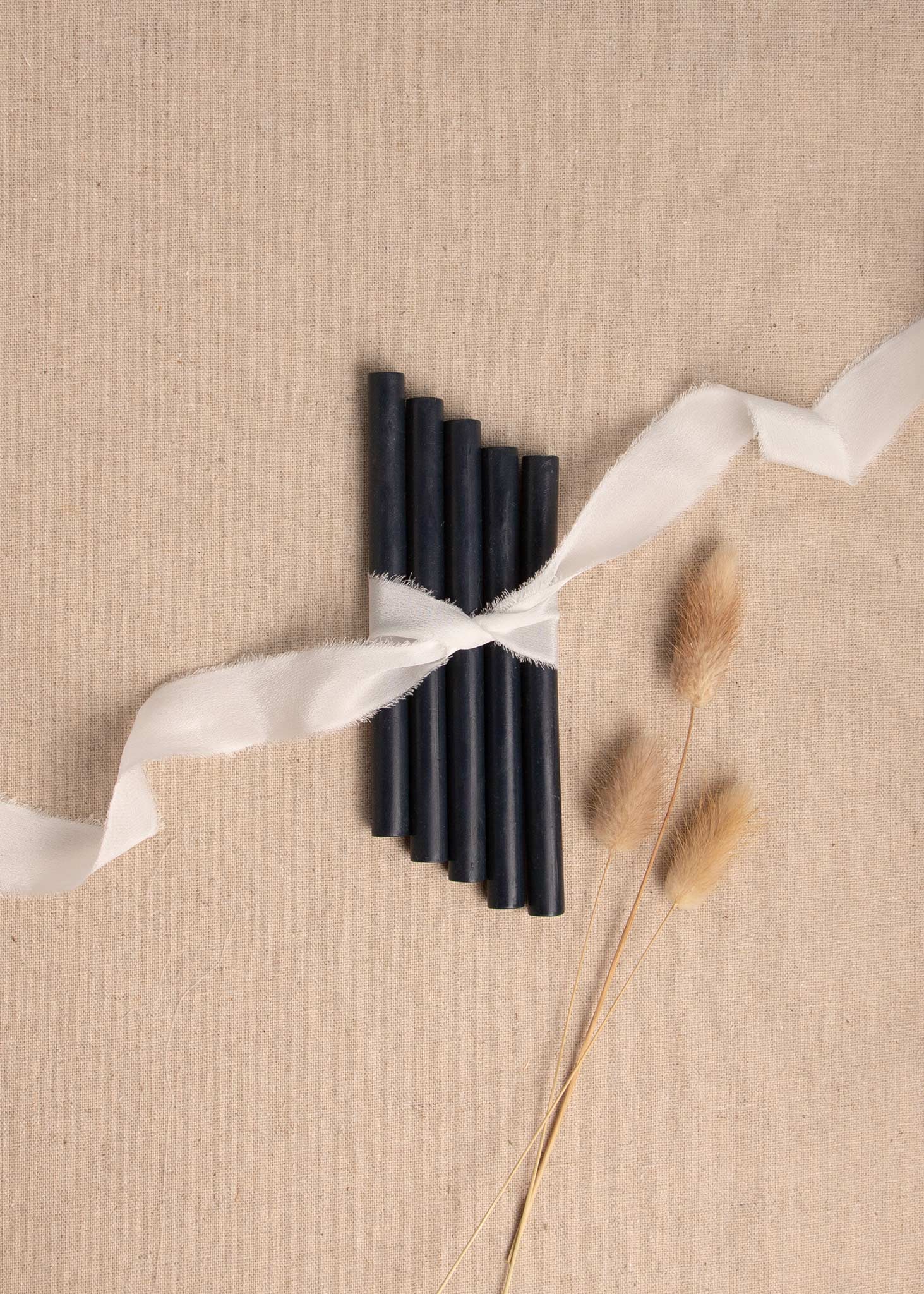 Dark blue wax sealing sticks on linen background with white silk ribbon and dried flowers