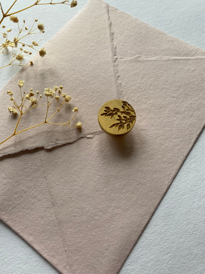 Leaf wax stamper on blush handmade paper surrounded by dried flowers