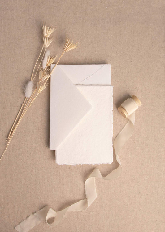 Matching Ivory handmade paper sheet and envelope with deckle edge surrounded by dried flowers and cream silk ribbon spool