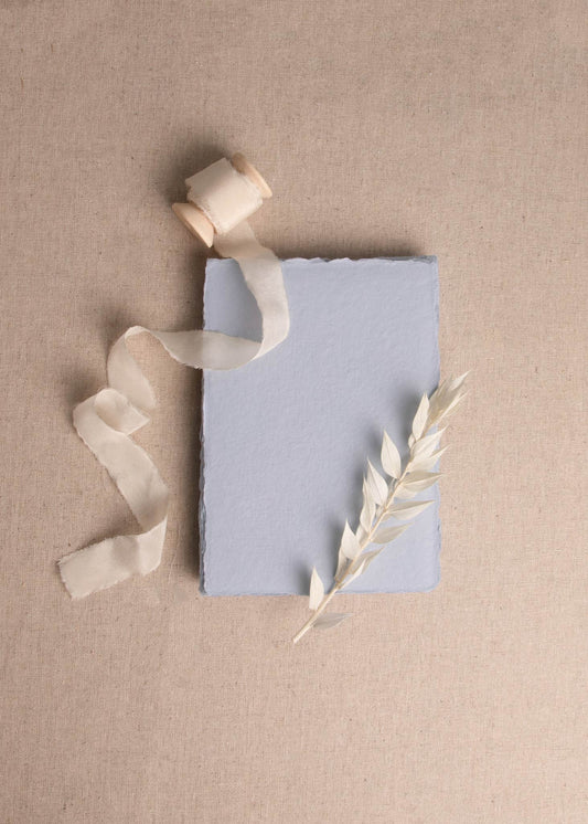 Fanned pile of Light Blue, Dusky Blue, Dark Blue handmade paper with deckle edge surrounded by dried flowers