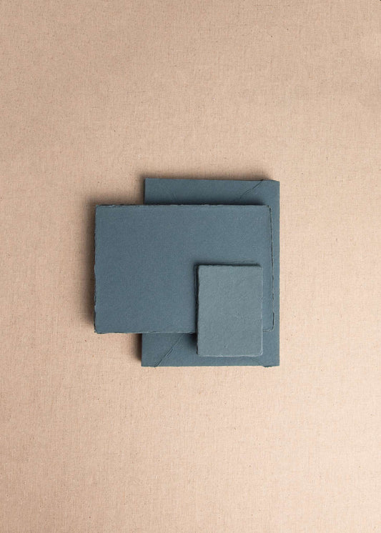 Pile of various sizes of Teal handmade paper with deckle edge on linen background