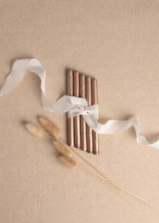 Cool bronze wax sealing sticks on linen background with silk white ribbon and dried flowers