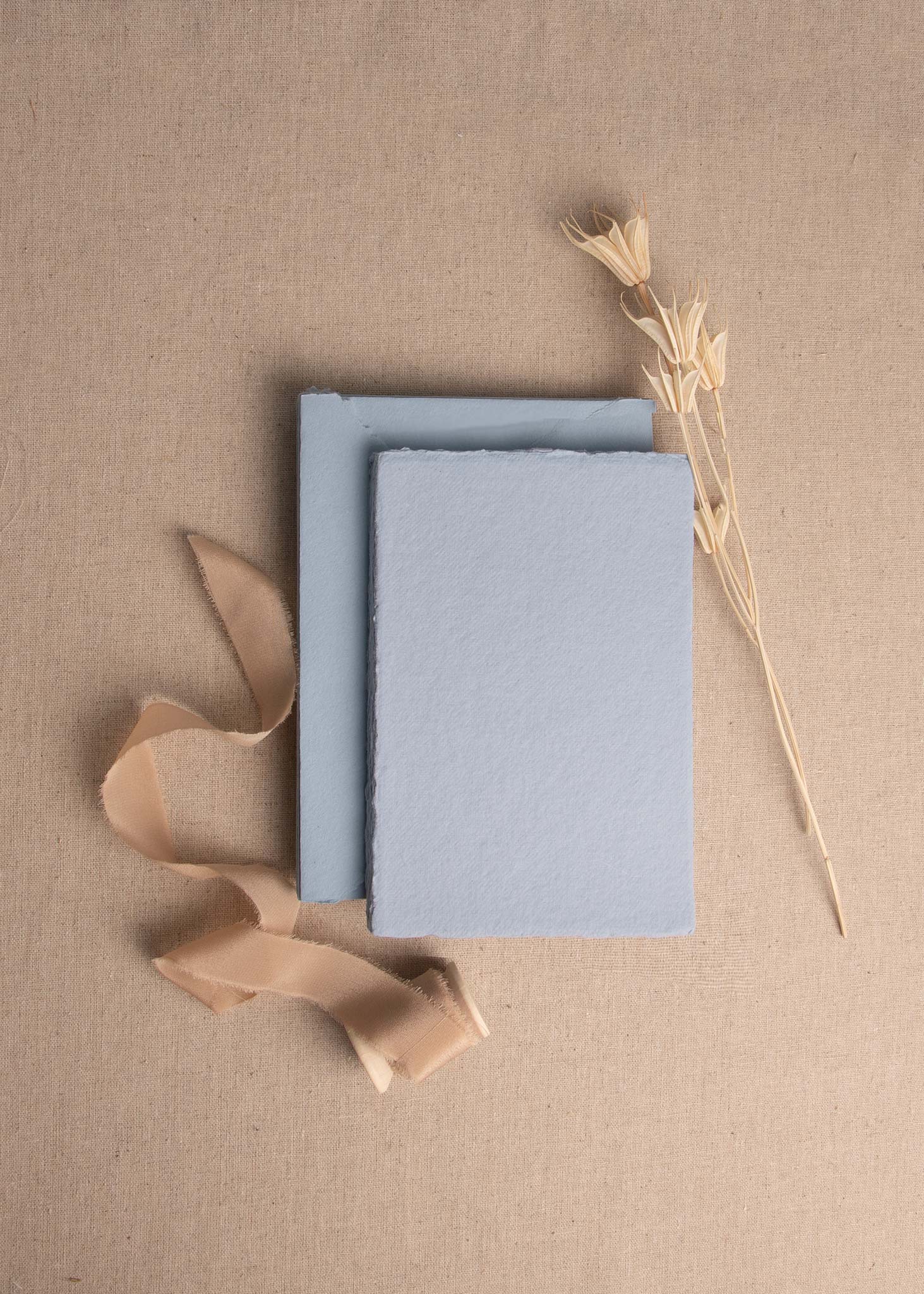 A6 Dusky Blue Handmade paper sheet with deckle edge surrounded by dried flowers and Caramel silk ribbon spool