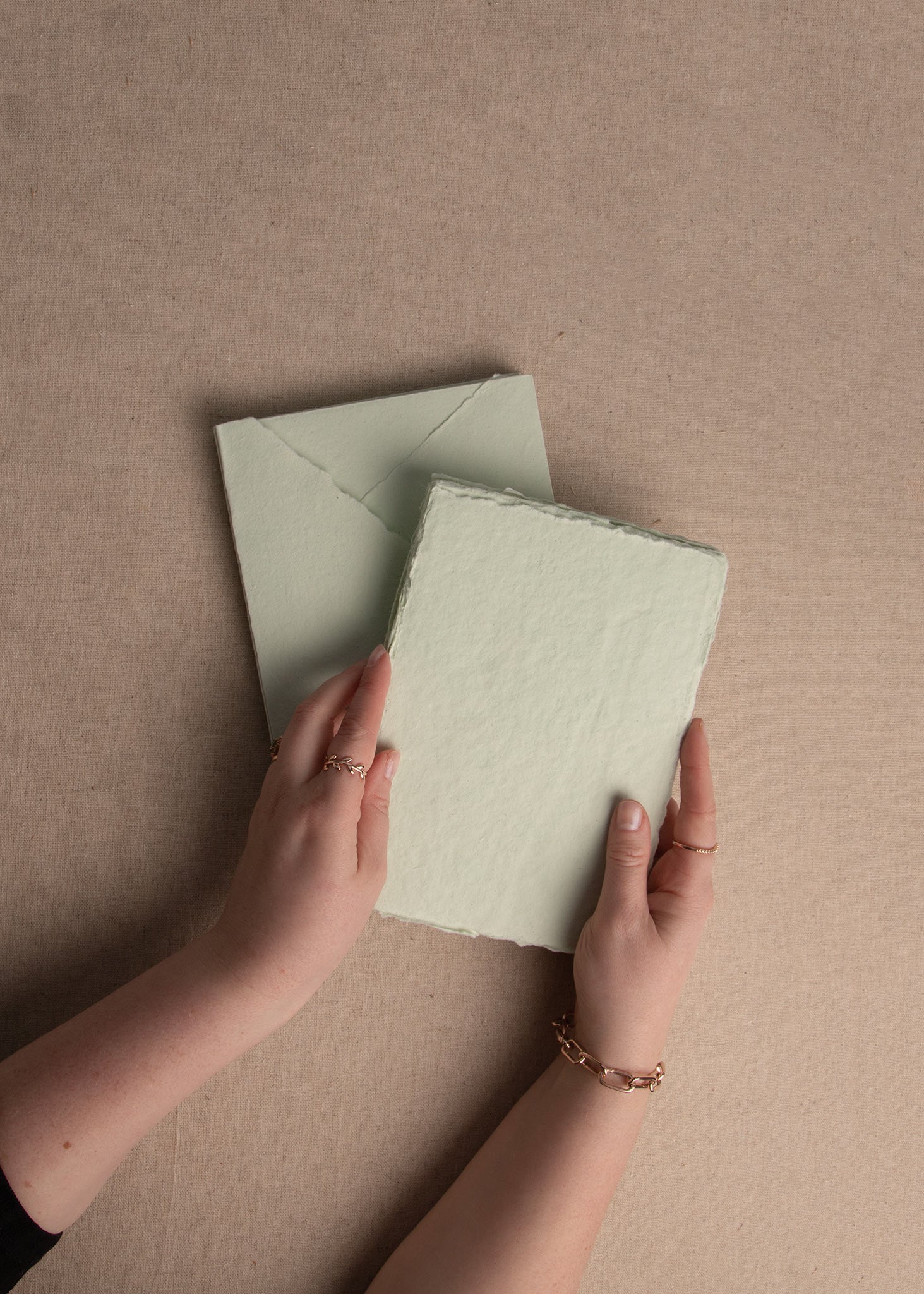 Elevated view of woman’s hand holding Mint Green 5x7 inch handmade paper sheet with deckle edge and matching envelope