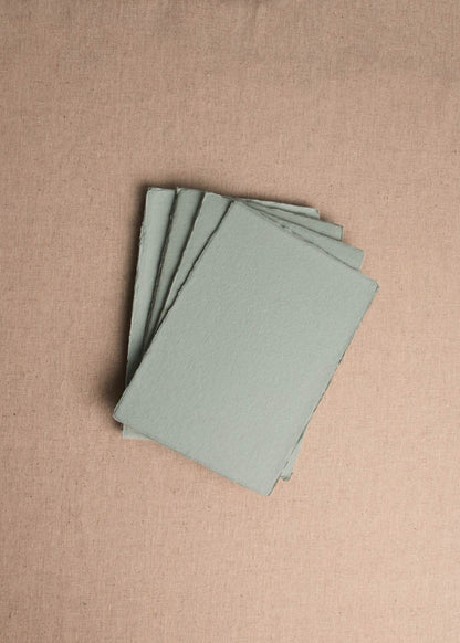 Fanned pile of Jade Green handmade paper with deckle edge on linen background