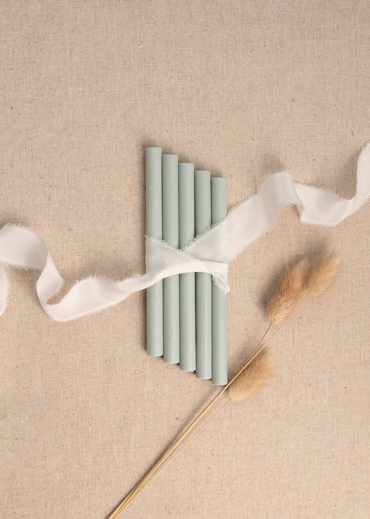 Muted sage wax seal sticks tied together with white ribbon and dried flowers 