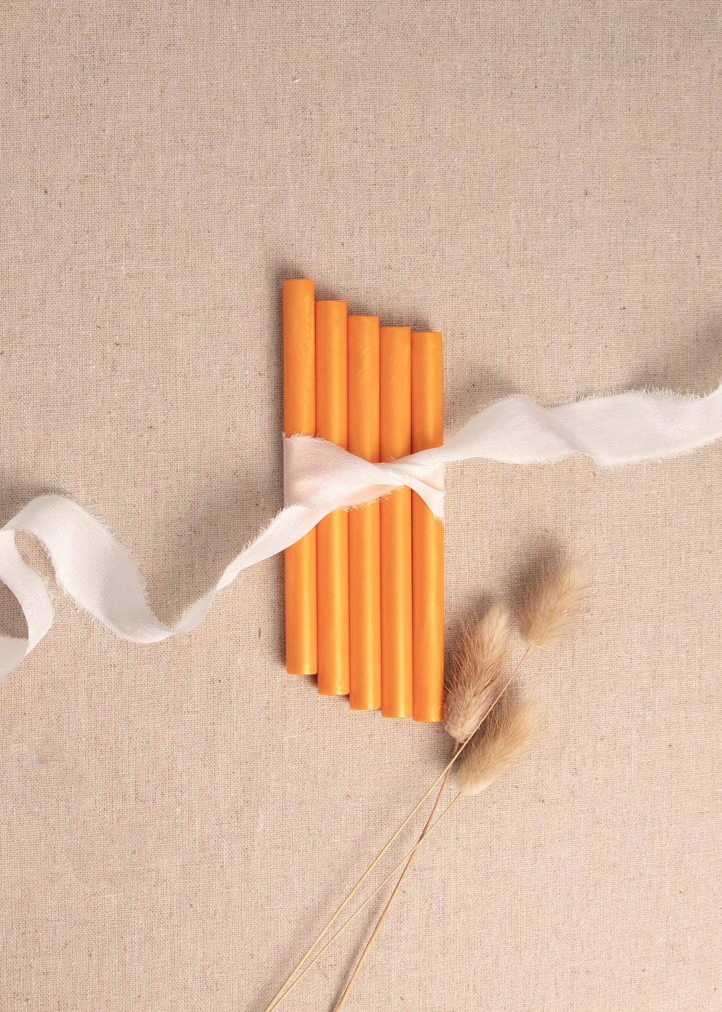 Orange wax seal sticks tied together with white ribbon and dried flowers 