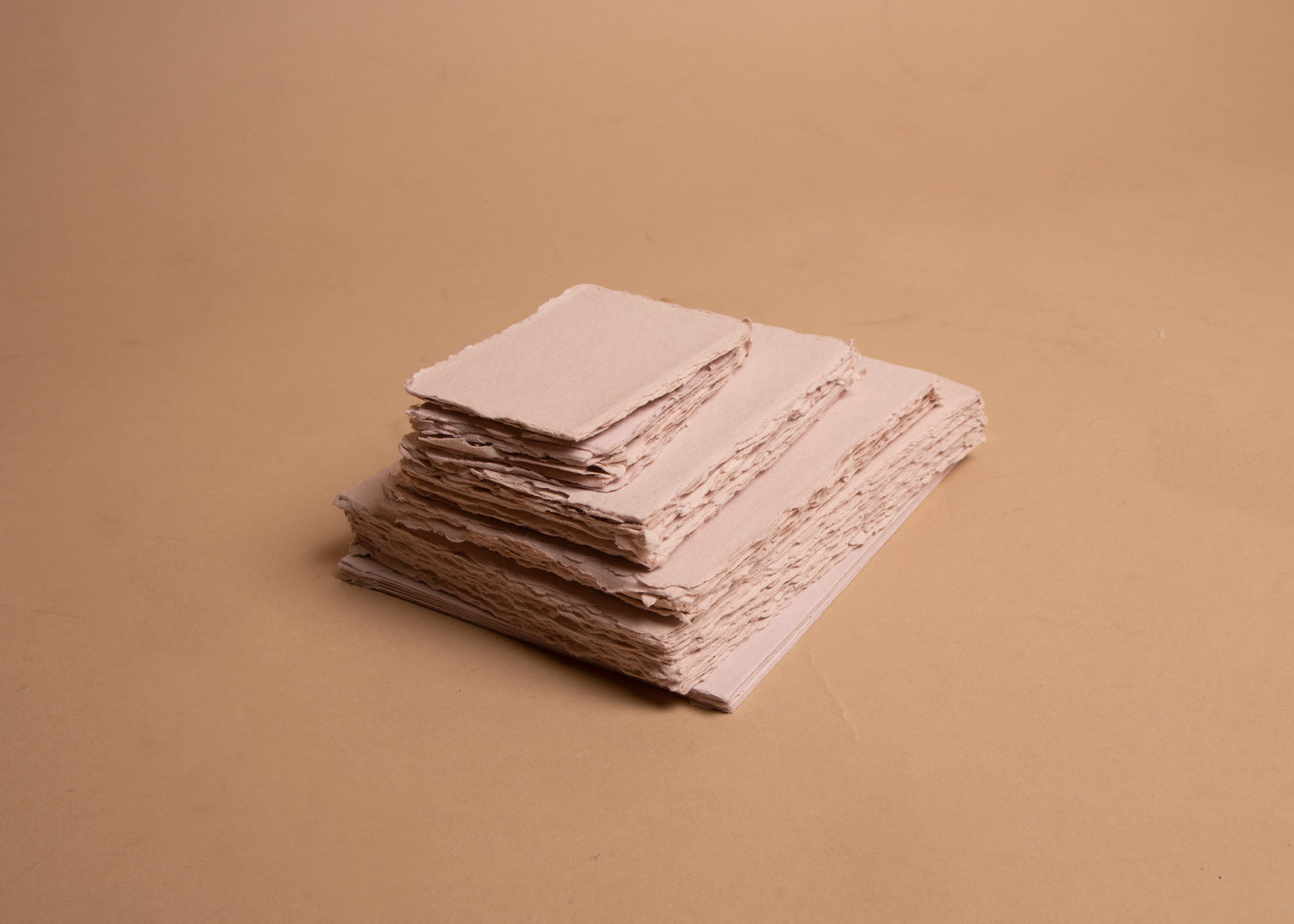 Stack of various sized blush handmade paper sheets and envelopes with deckle edge