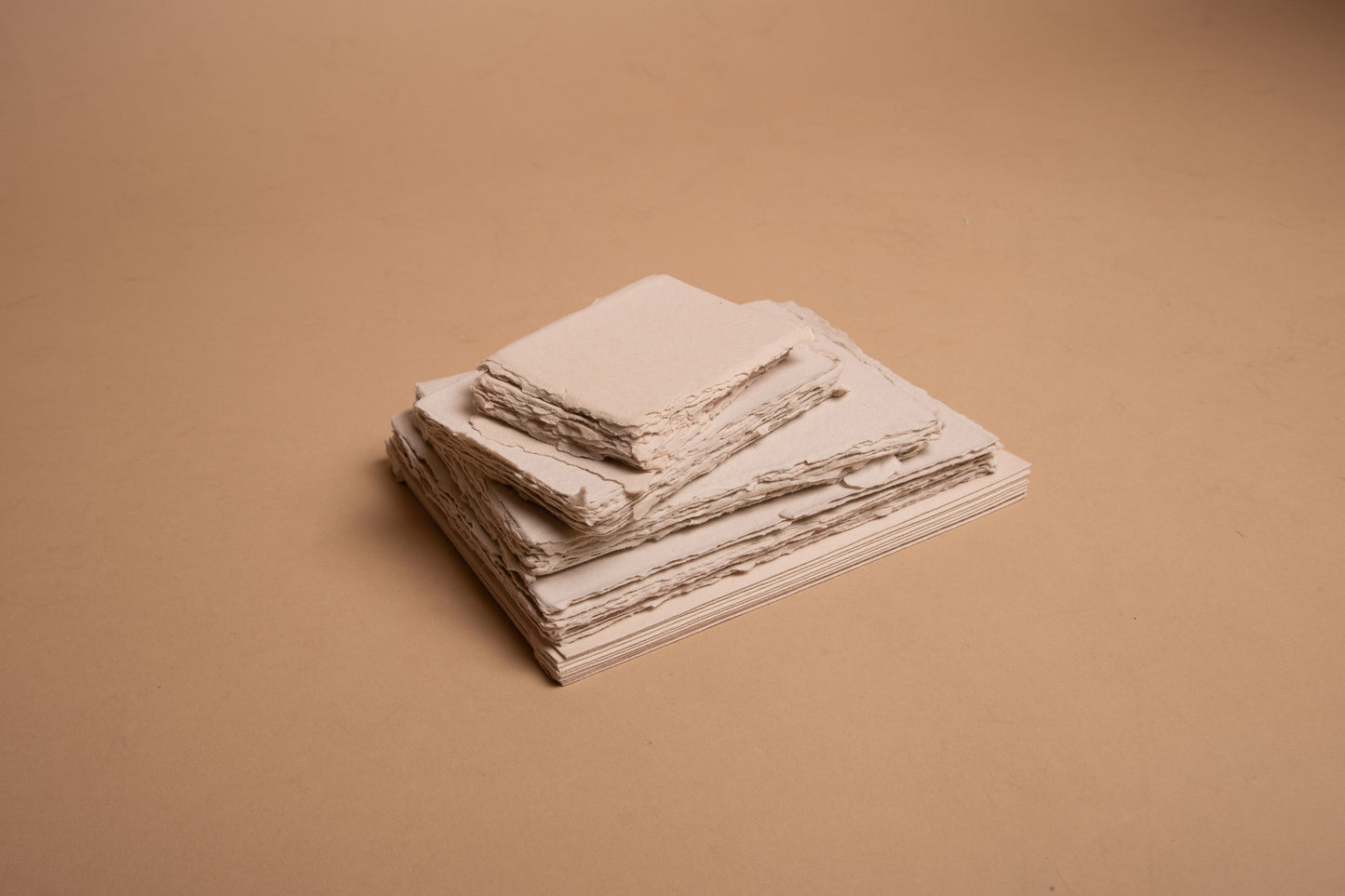 Stack of various sized beige handmade paper sheets and envelopes with deckle edge