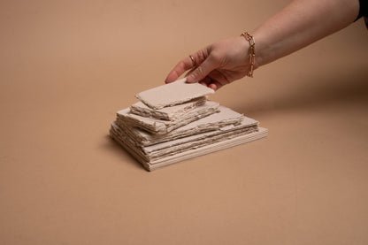 Woman’s hand and stack of various sized beige handmade paper and envelopes with deckle edge