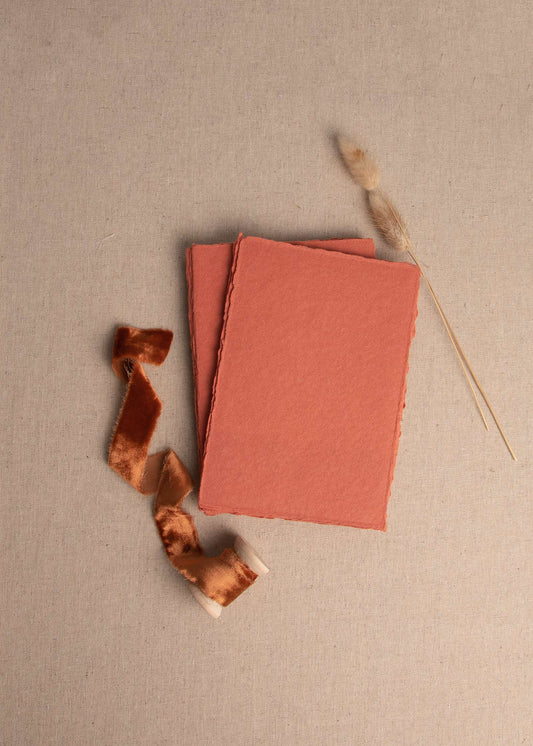  5x7 inch Sunset Red Handmade paper sheet with deckle edge surrounded by dried flowers and Terracotta velvet ribbon spool