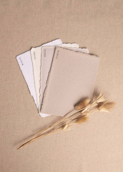 Fanned pile of White, Ivory, Beige, Earth handmade paper with deckle edge surrounded by dried flowers