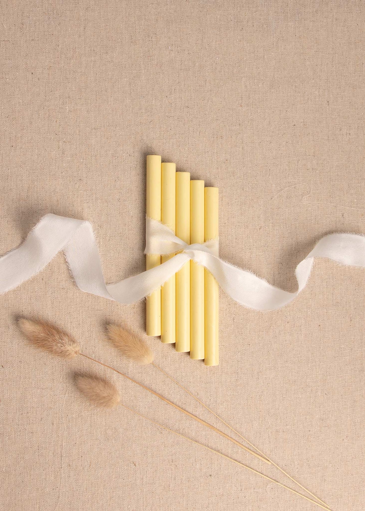 Yellow wax seal sticks tied with white silk ribbon on linen background with dried flowers