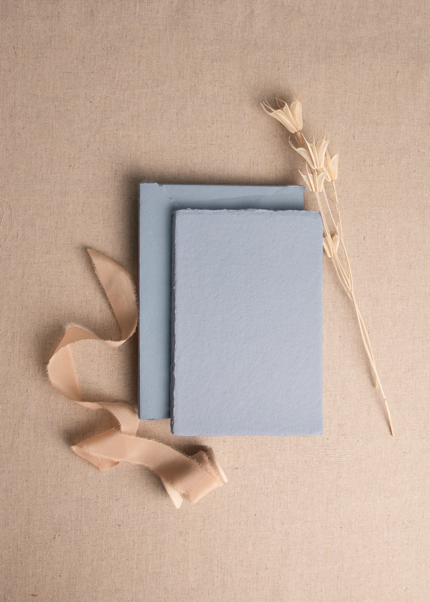 A6 Dusky Blue Handmade envelope and paper sheet with deckle edge surrounded by dried flowers and Caramel silk ribbon spool