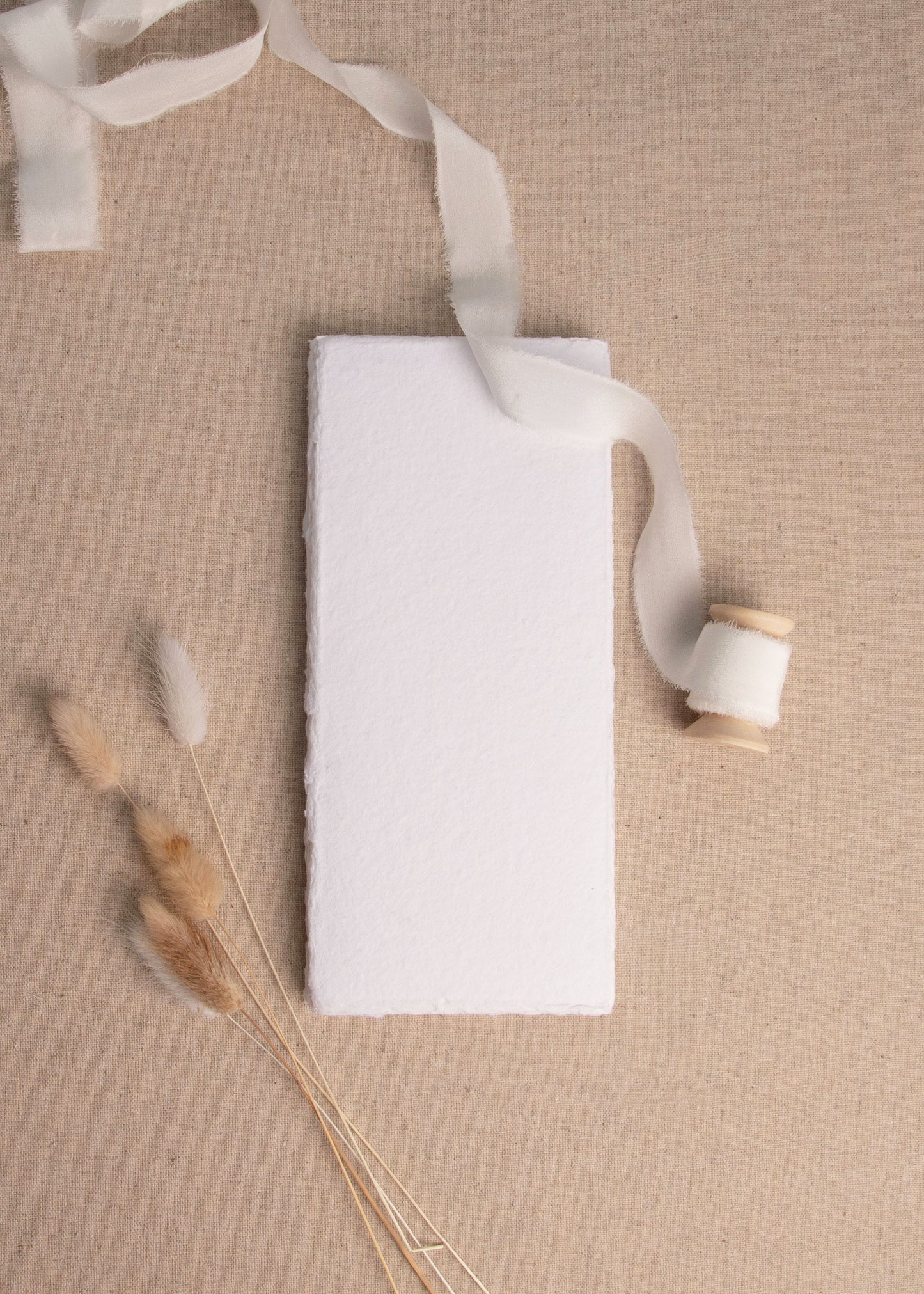 Menu size White handmade paper with deckle edge surrounded by dried flowers and white ribbon spool