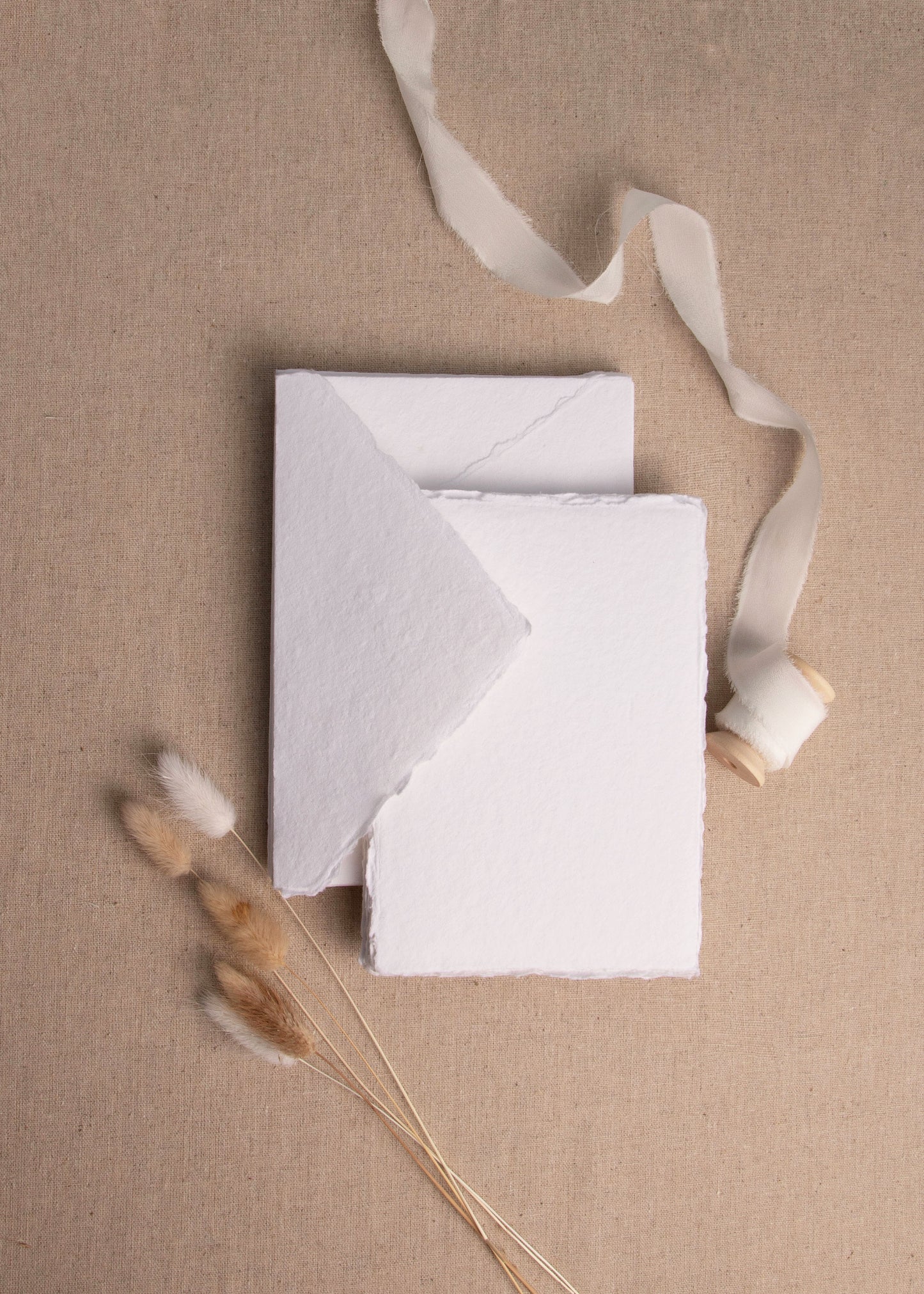 Matching White handmade paper envelope and sheet with deckle edge surrounded by white silk ribbon spool and dried flowers